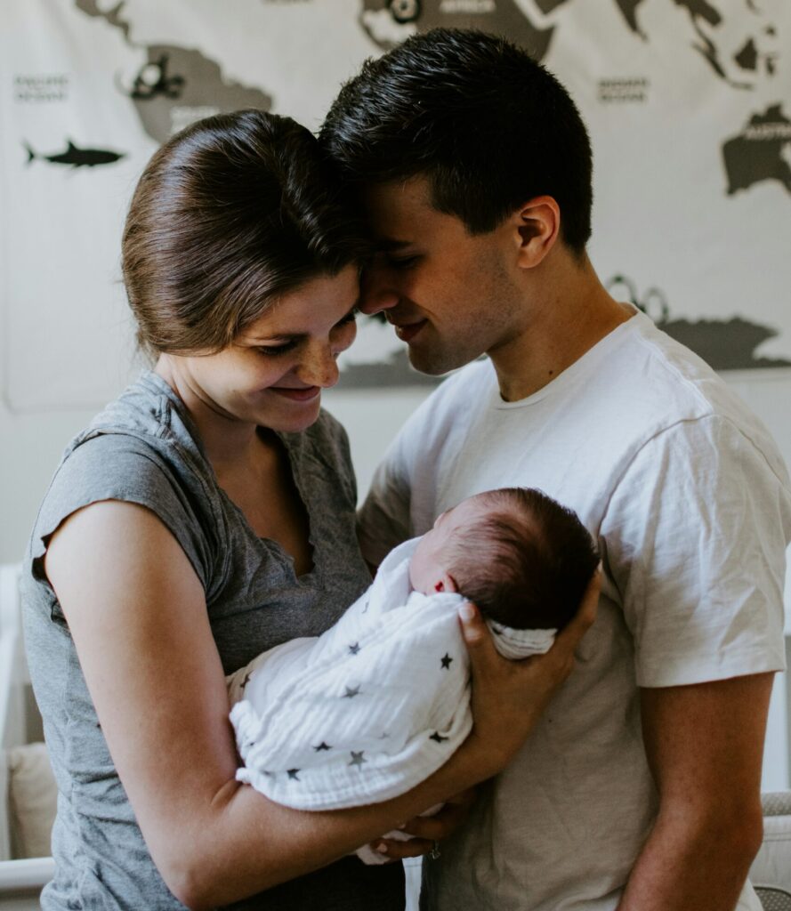 Une jeune mère allaitante regarde son bébé avec douceur et tendresse, le papa est présent au coté de la maman pour la soutenir près a la soutenir grâce a l'accompagnement de leur conseillère en lactation